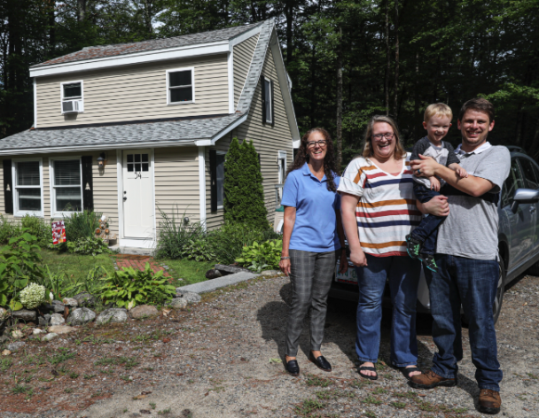 Family and Realtor stand in driveway smiling with home in background